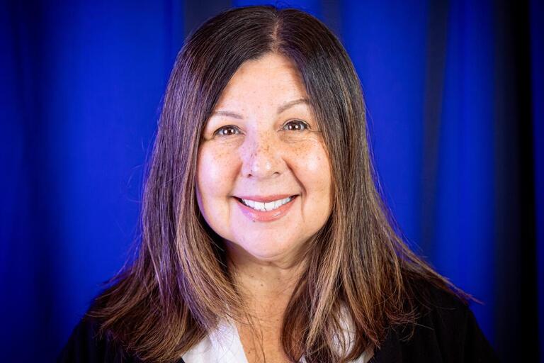 Professional headshot of a female, in front of a navy blue background