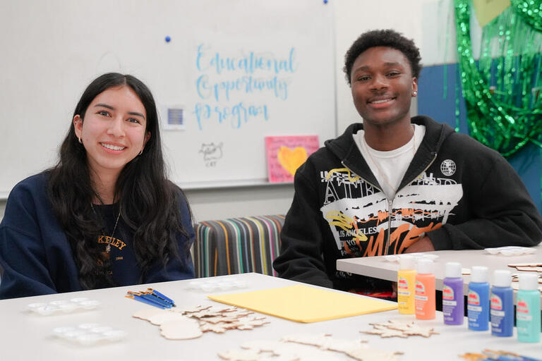 Two students sitting at a table, engaged in arts and crafts, surrounded by colorful supplies.
