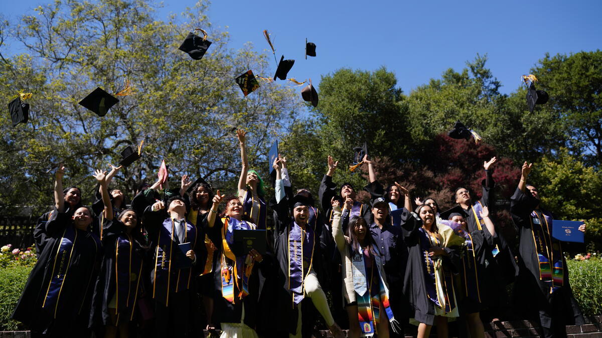 Students in graduation gowns throwing their graduation caps in the air.